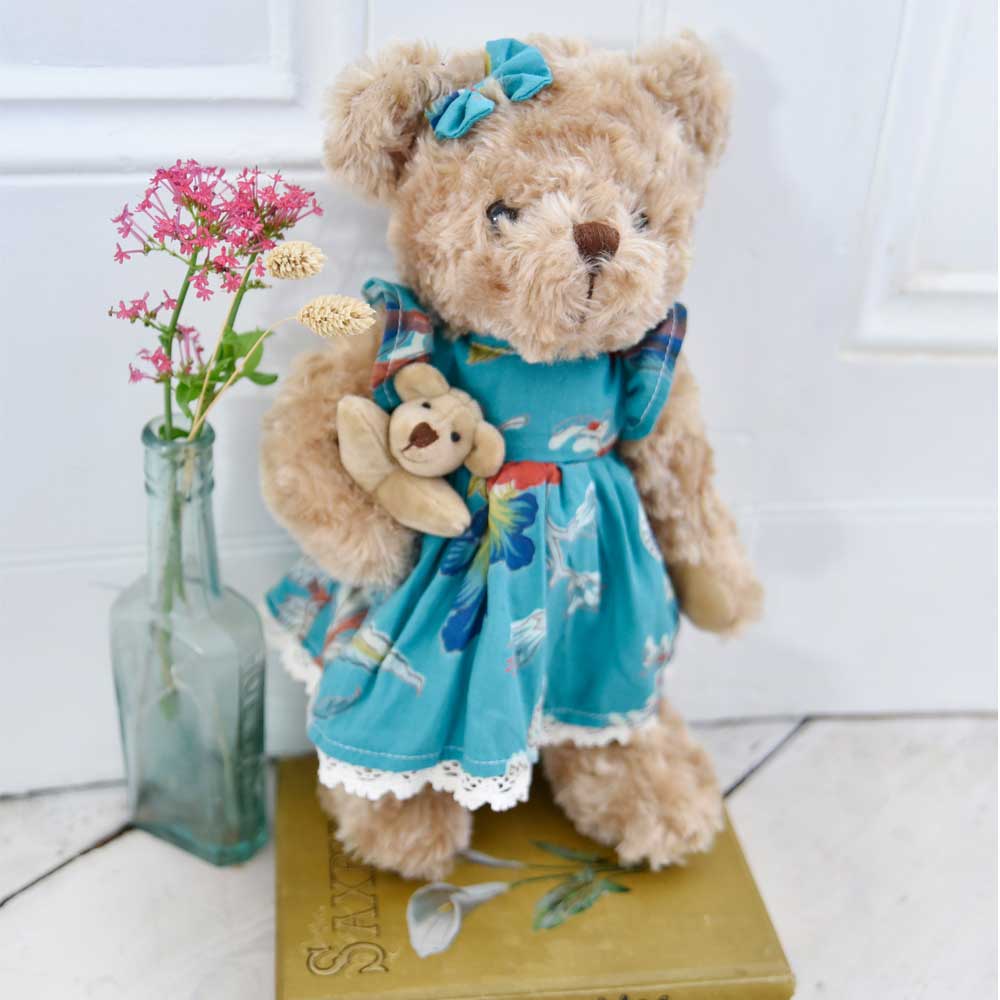 Teddybär mit blaugrünem Kleid mit exotischem Aufdruck und Baby